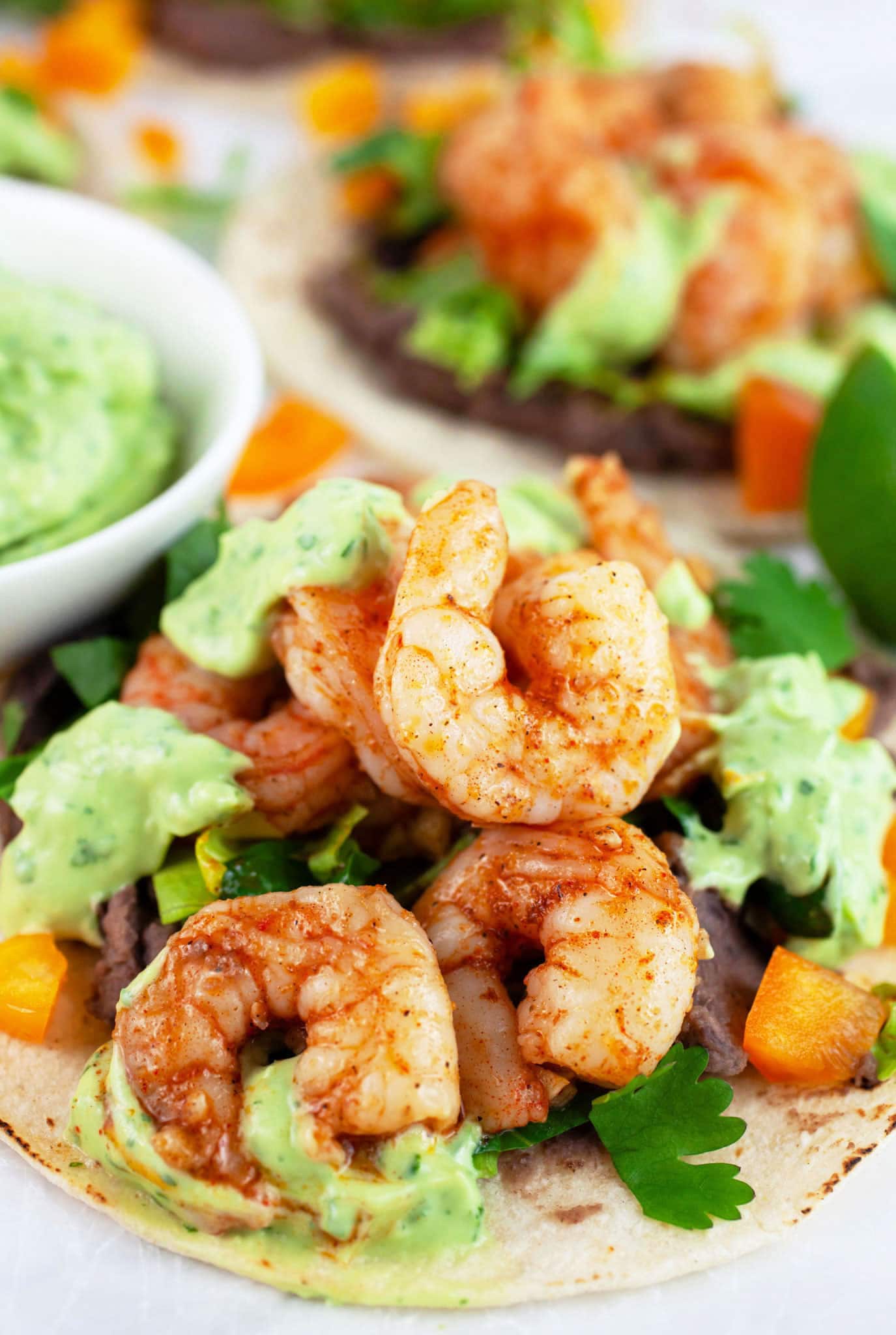 Cajun shrimp tacos on corn tortillas drizzled with avocado sauce.