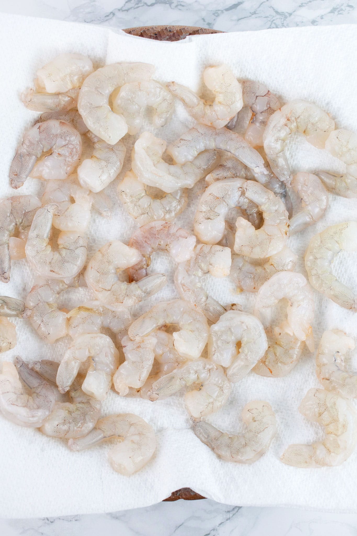 Raw shrimp on plate lined with paper towels.