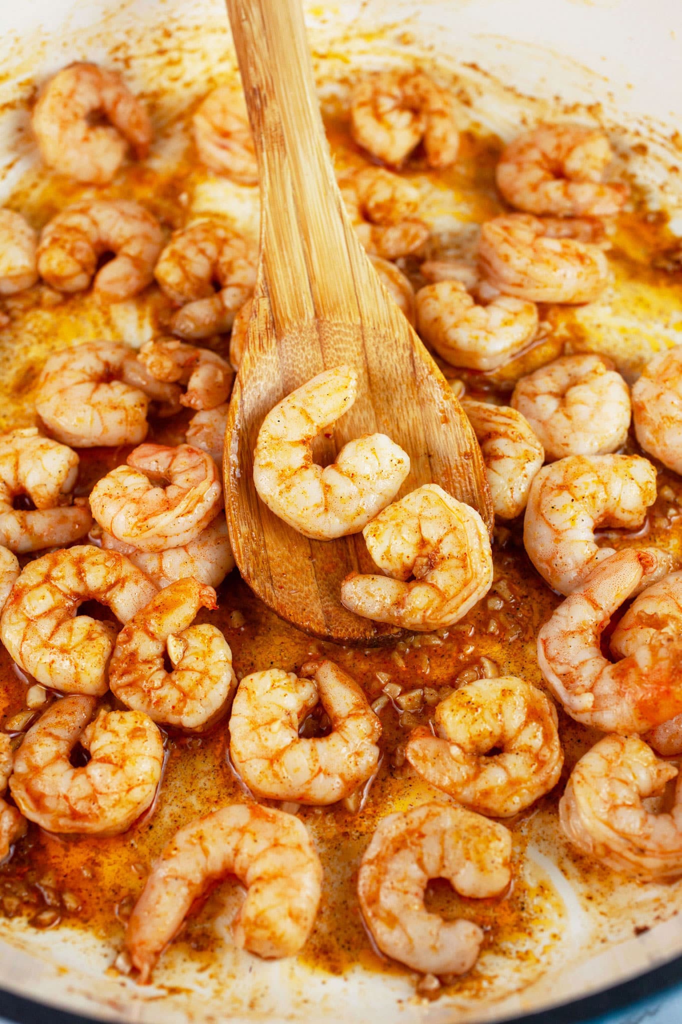Shrimp sauteed in Cajun spices in skillet with wooden spatula.