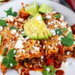 Ground beef enchiladas garnished with cilantro, avocado, and Queso fresco on white plate with fork.