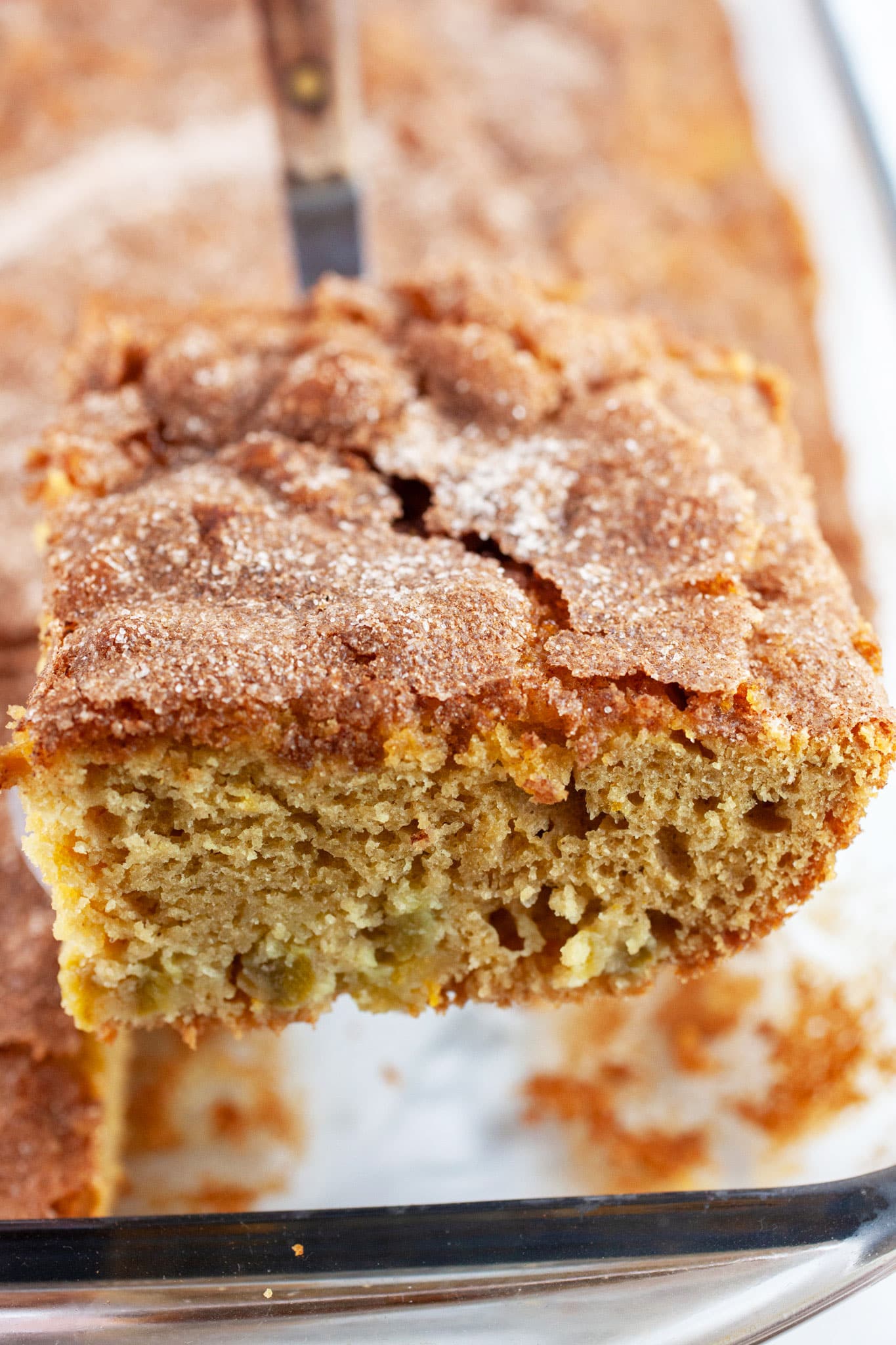 Piece of rhubarb cake lifted on spatula from glass baking dish.