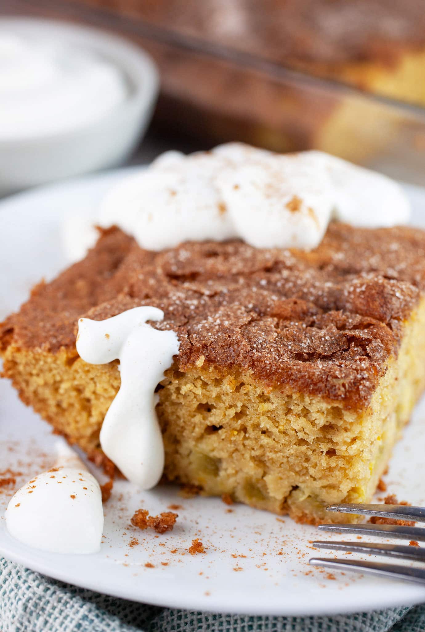 Piece of gluten free rhubarb cake topped with whipped cream on white plate with fork.