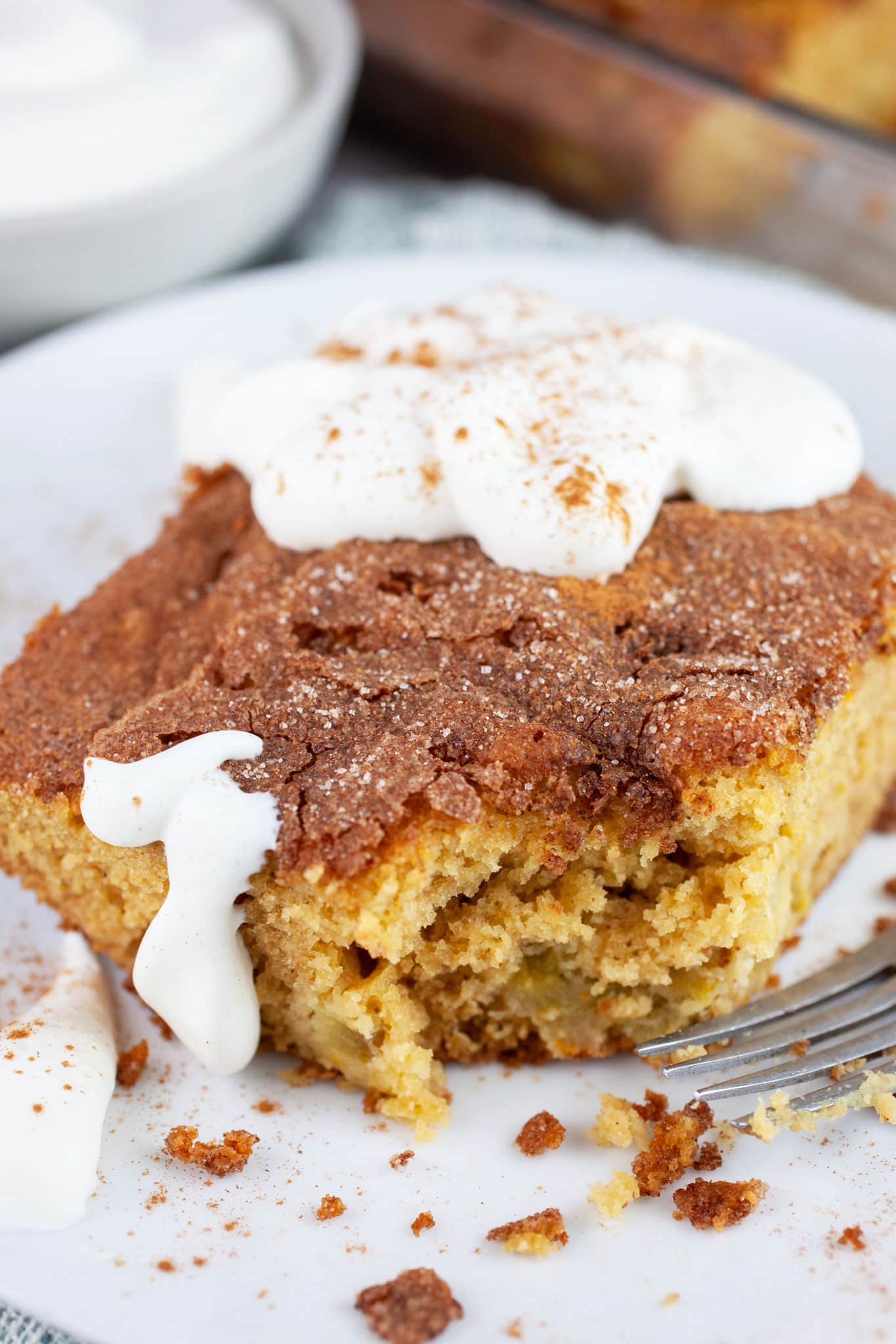 Piece of rhubarb cake with bite taken topped with whipped cream on white plate with fork.