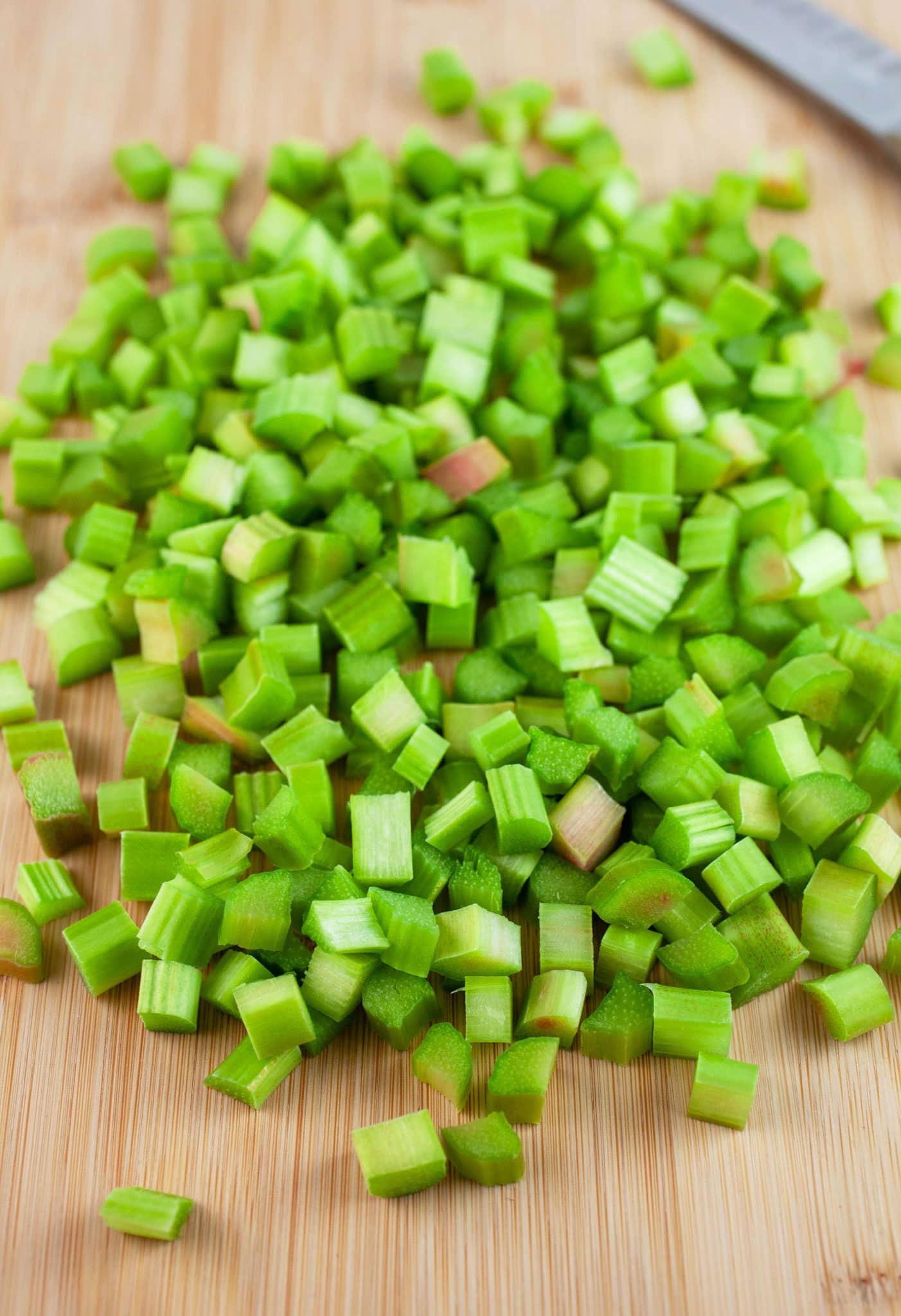 Diced fresh rhubarb on wooden cutting board with knife.