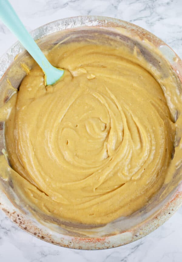 Wet and dry ingredients combined in ceramic bowl with blue spatula.