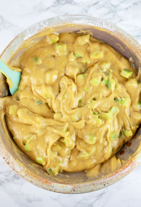 Rhubarb cake batter in ceramic bowl with blue spatula.
