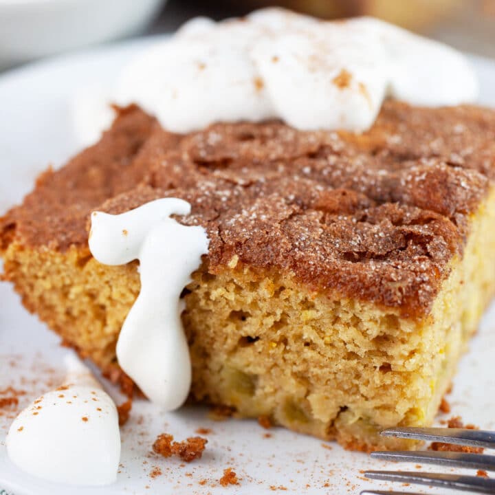 Piece of gluten free rhubarb cake with whipped cream on white plate with fork.