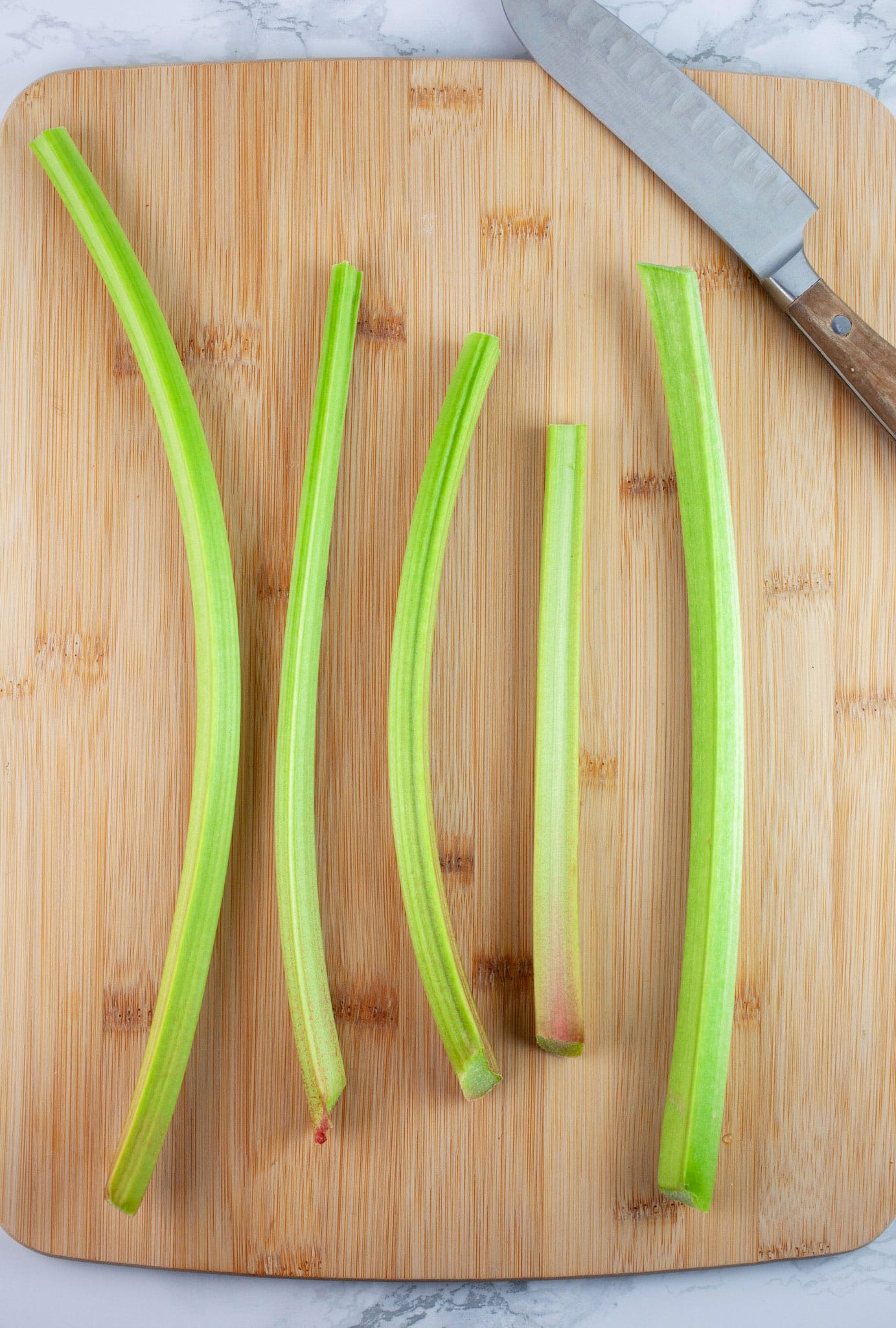 Stalks of fresh rhubarb on wooden cutting board with knife.