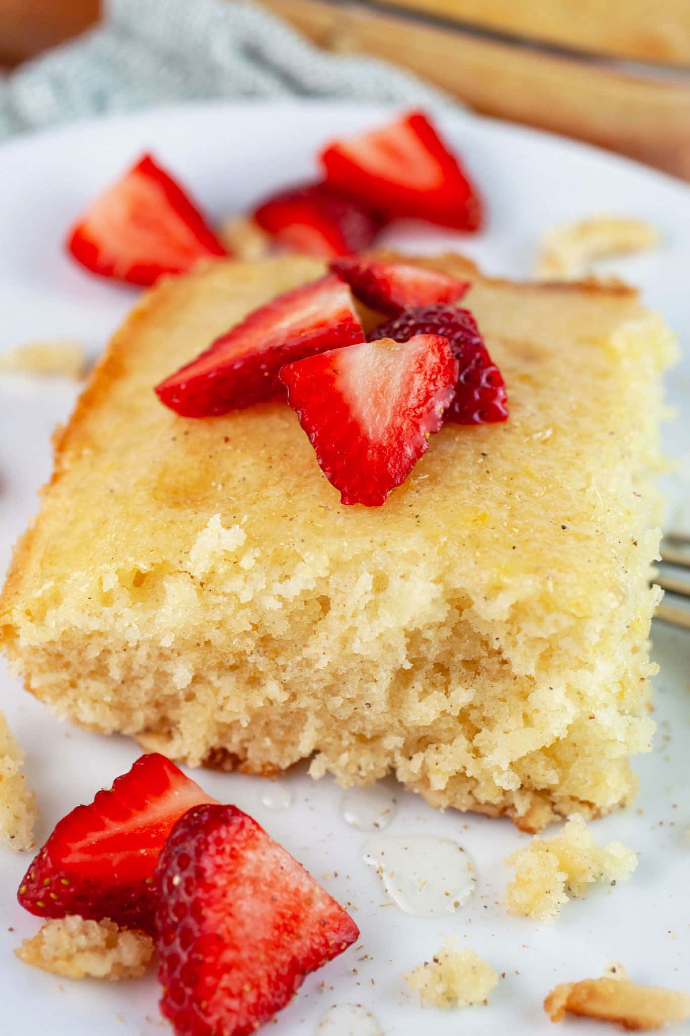 Slice of lemon cardamom cake with fresh strawberries on white plate with fork.