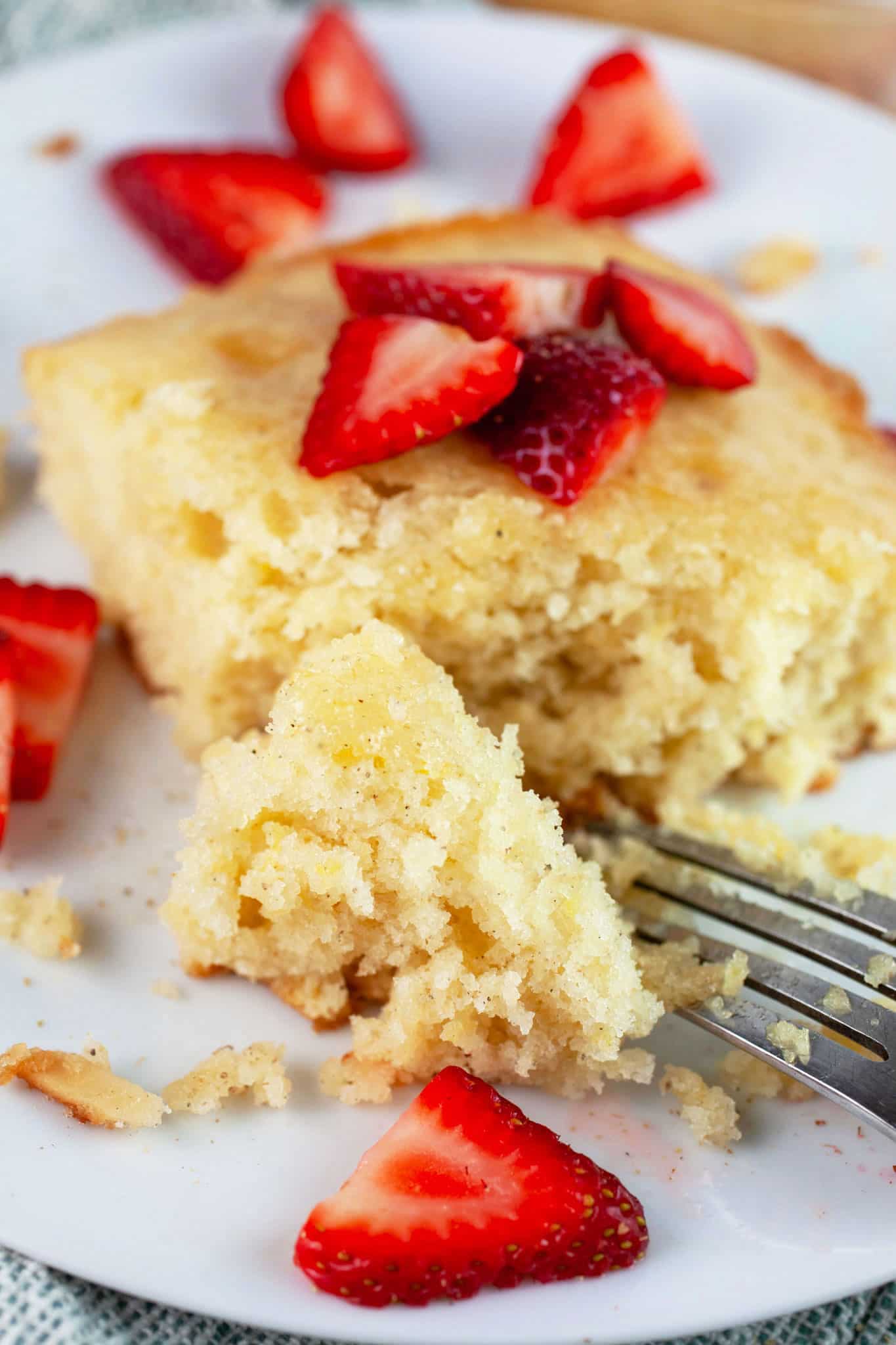 Lemon cardamom cake with fresh strawberries on white plate with fork.