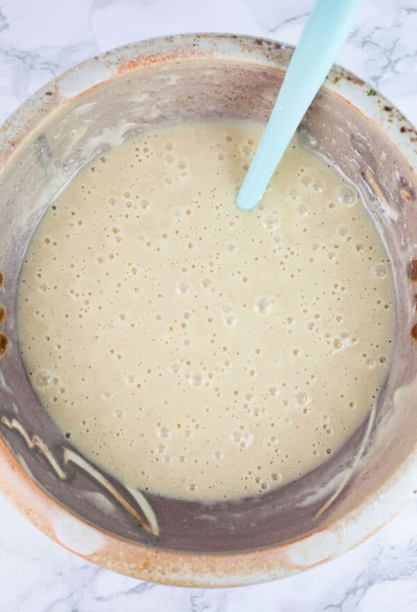 Wet and dry ingredients combined in ceramic bowl with spatula.