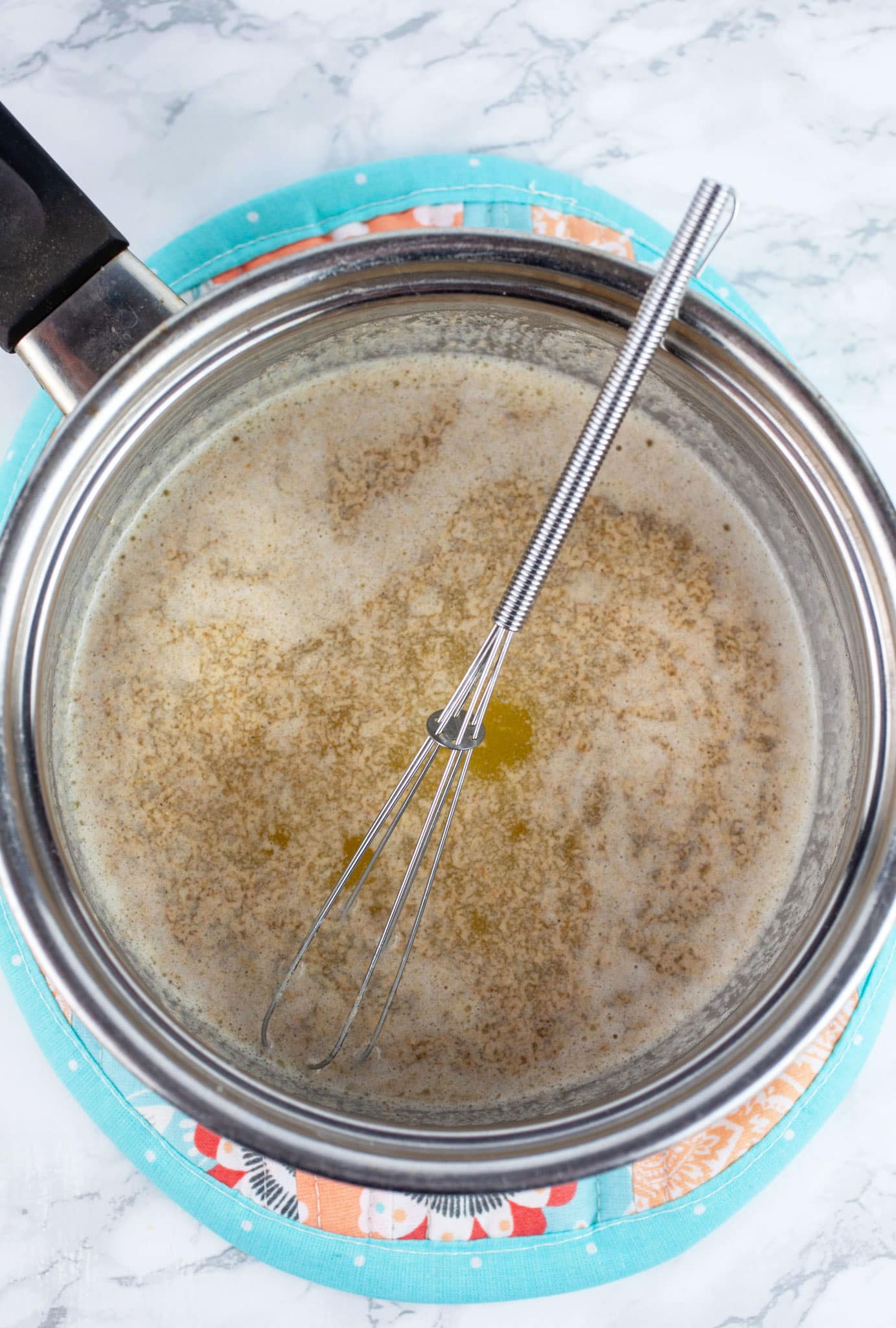 Melted butter with ground cardamom in sauce pan on potholder with small whisk.