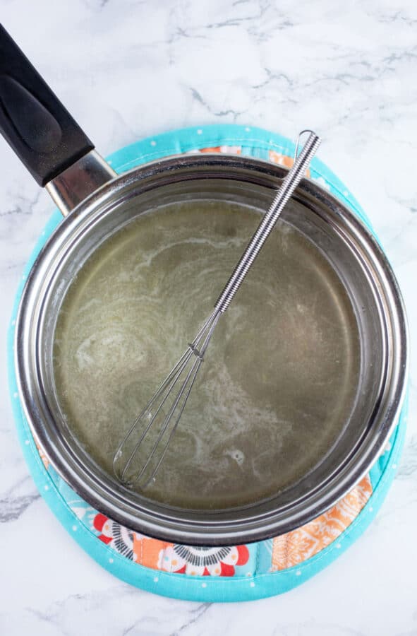 Lemon glaze in sauce pan on potholder with small whisk.