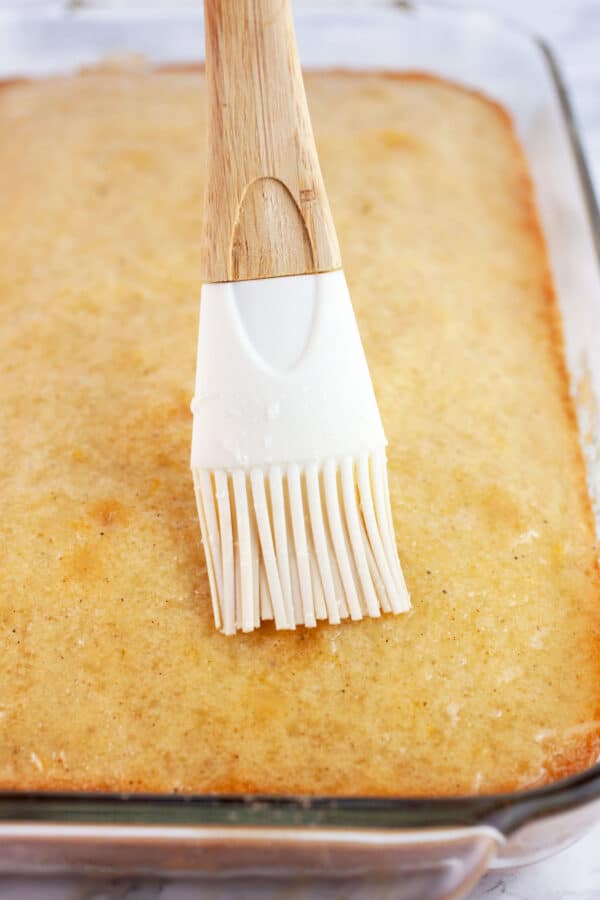 Lemon glaze brushed onto lemon cake in glass baking dish.