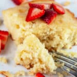 Lemon cardamom cake with fresh strawberries on white plate with fork.
