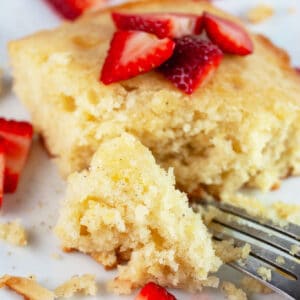 Lemon cardamom cake with fresh strawberries on white plate with fork.