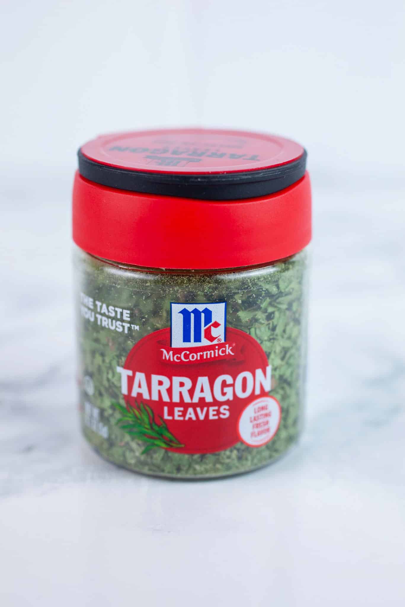 Unopened container of dried tarragon on white surface.