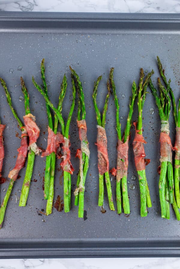 Roasted prosciutto wrapped asparagus on baking sheet.