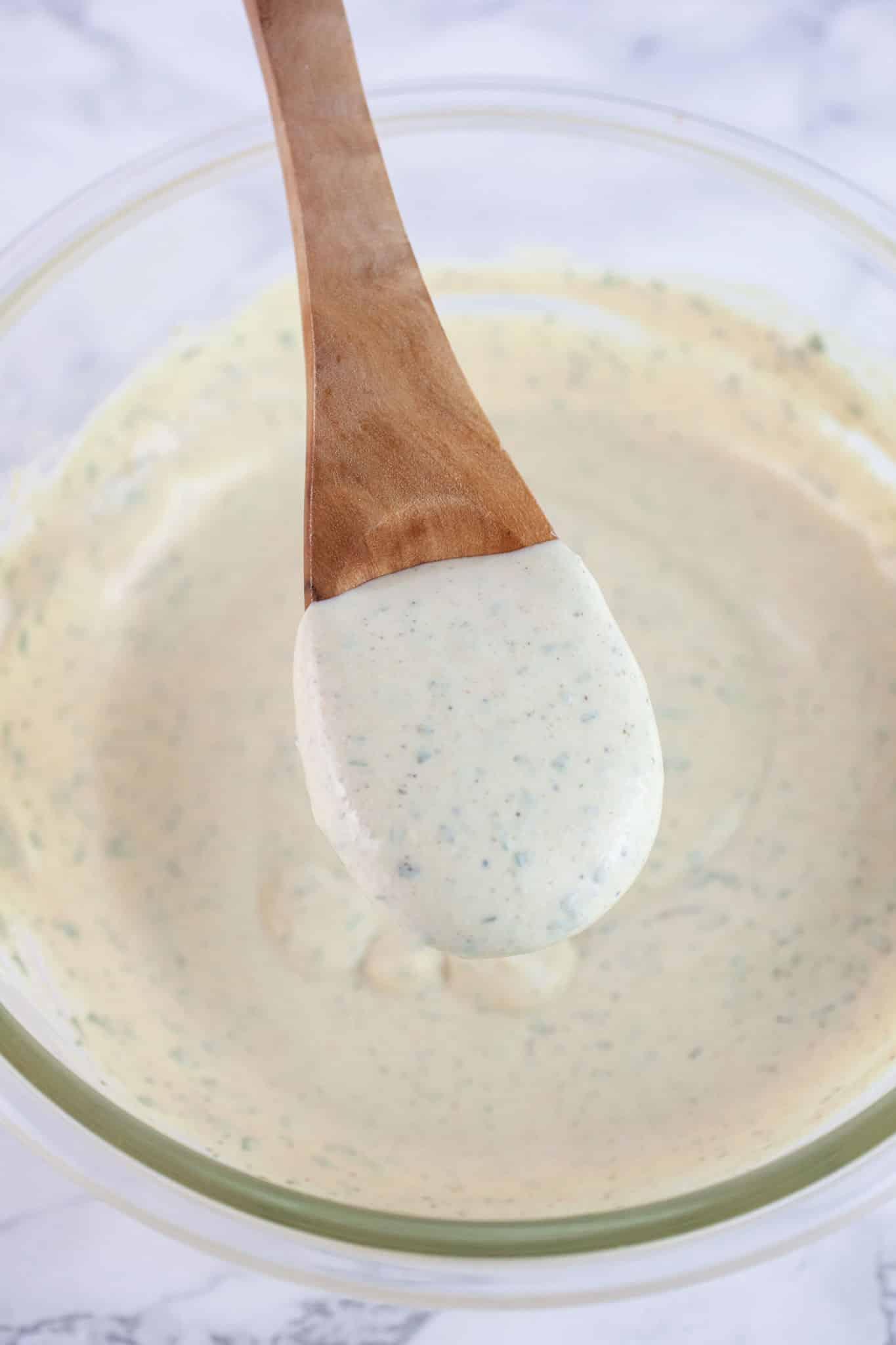 Wooden spoonful of creamy tarragon sauce lifted from small glass bowl.