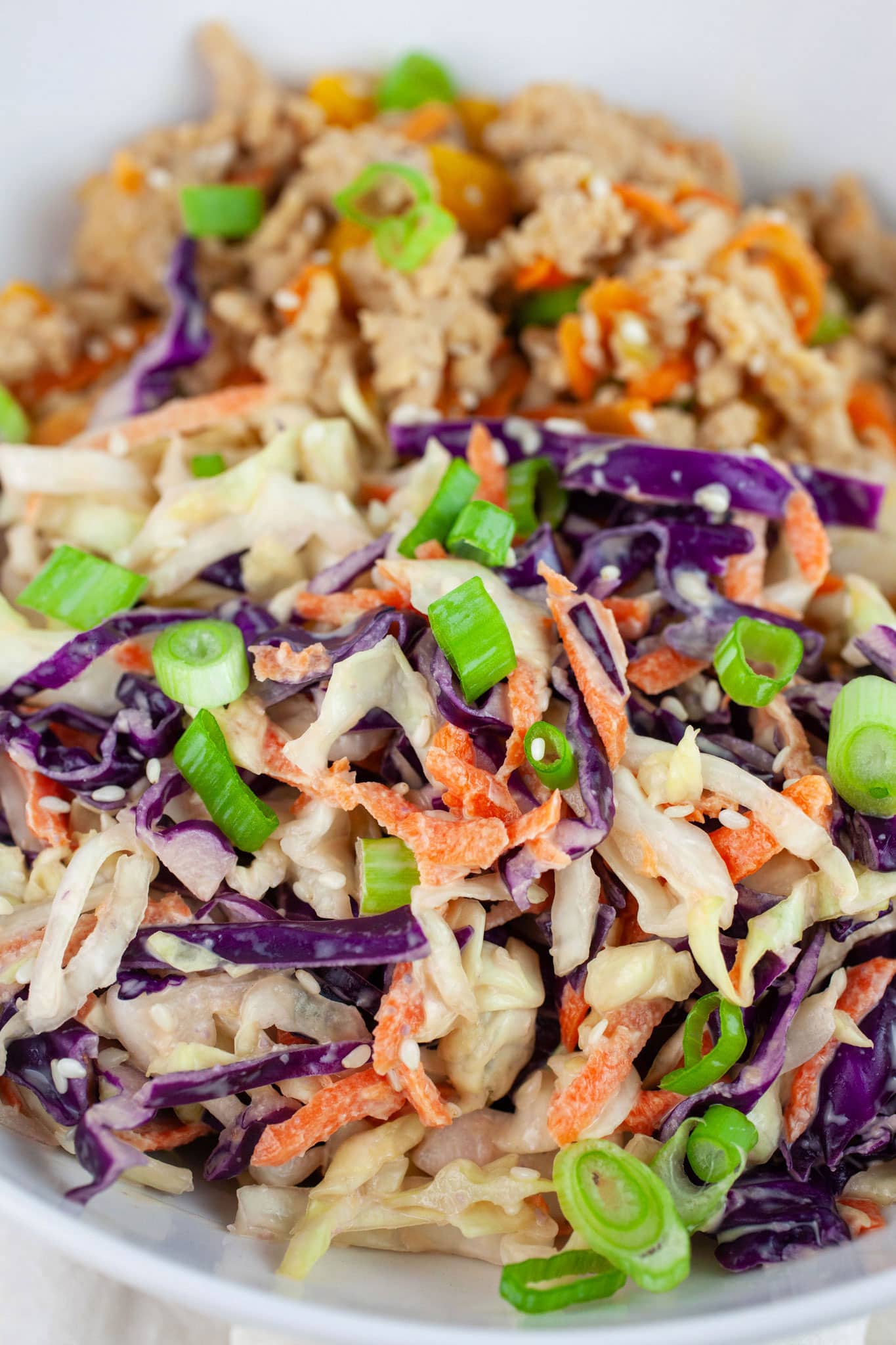Miso ginger coleslaw with ground Asian chicken garnished with green onions and sesame seeds in white bowl.