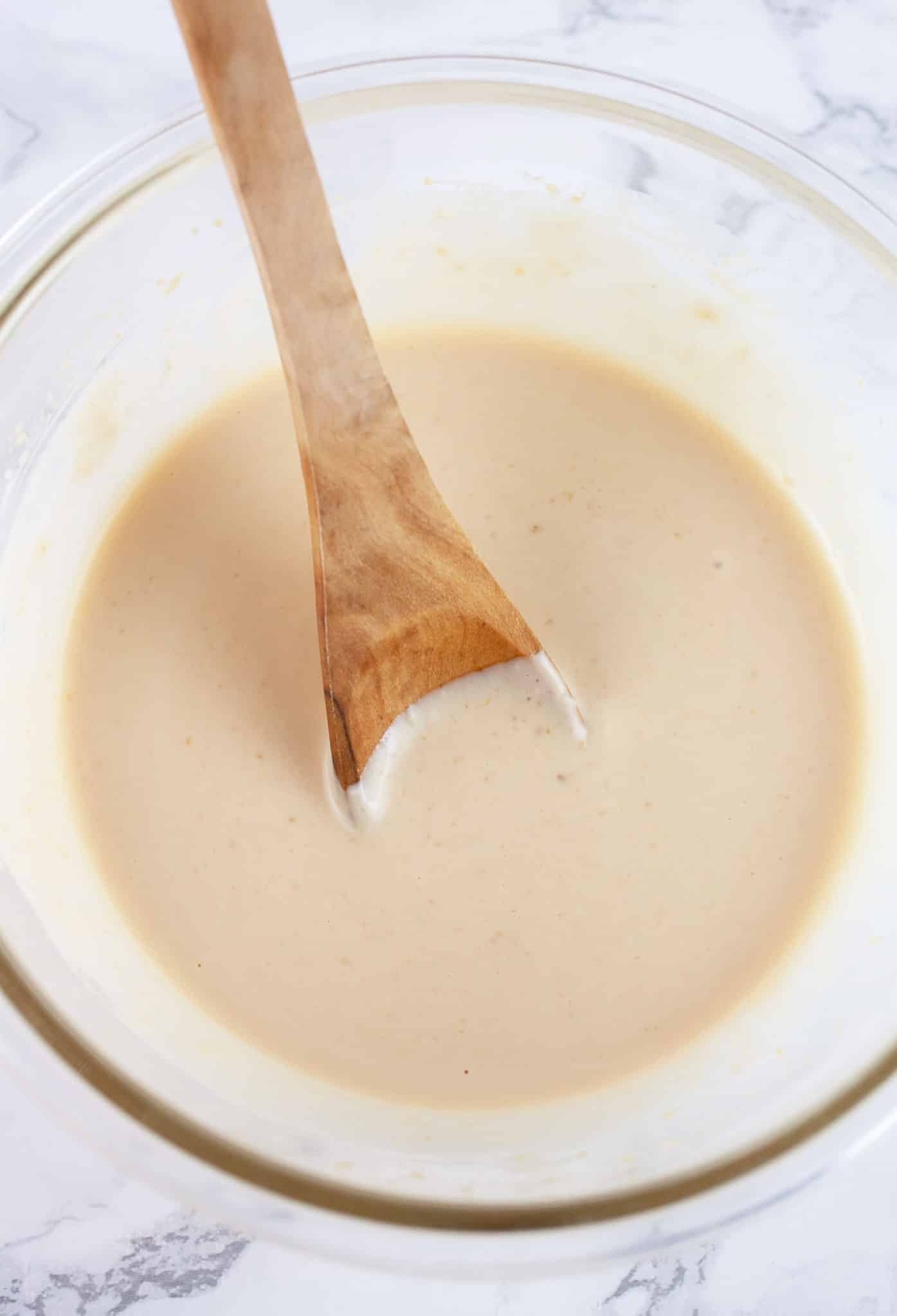 Miso ginger dressing in glass bowl with wooden spoon.