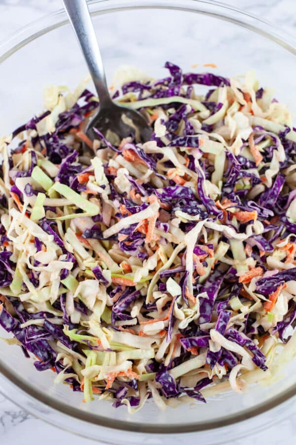 Asian cabbage slaw combined in glass mixing bowl with spoon.