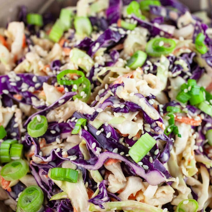 Asian cabbage slaw in ceramic bowl garnished with green onions and sesame seeds.