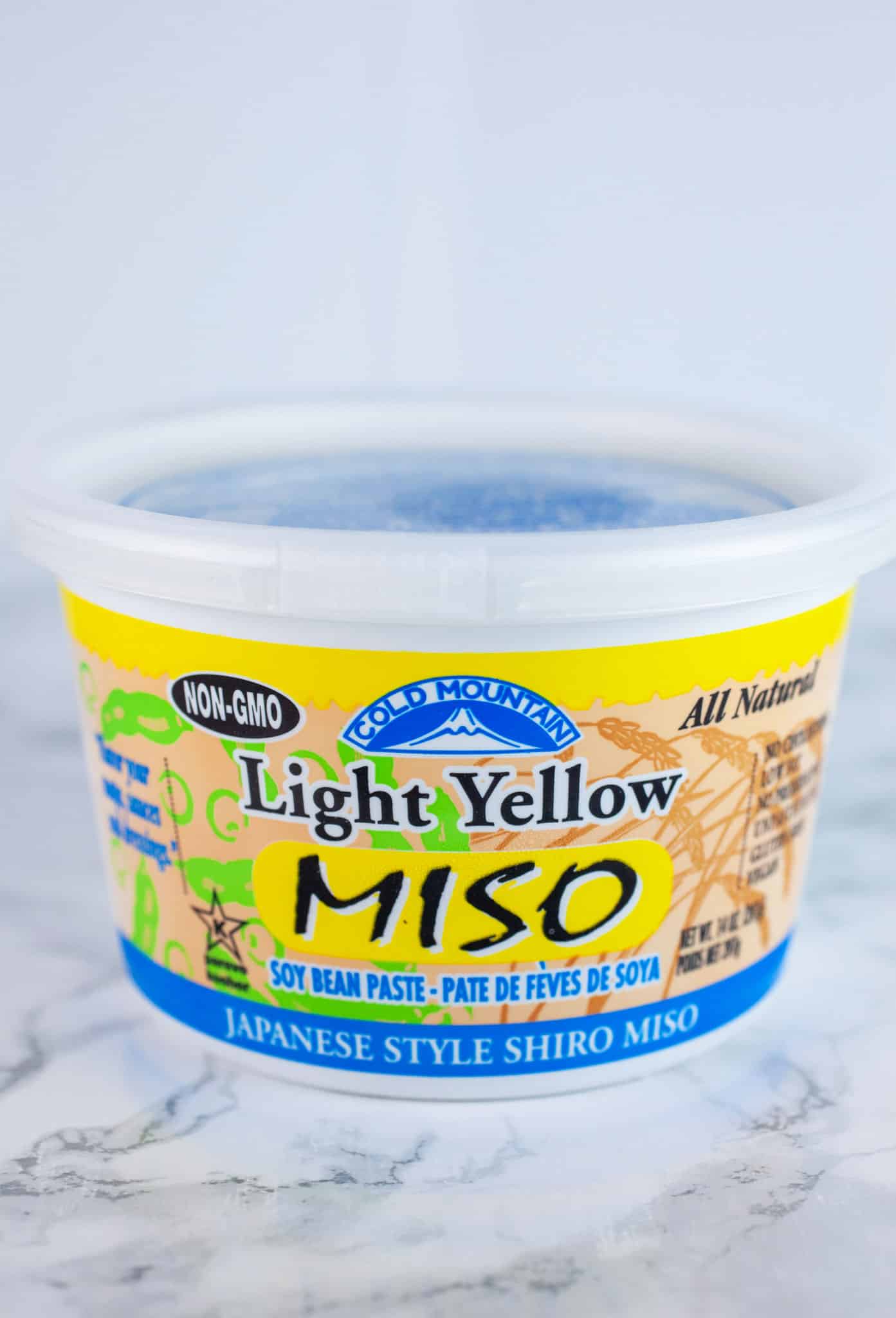 Unopened container of yellow miso on white surface.