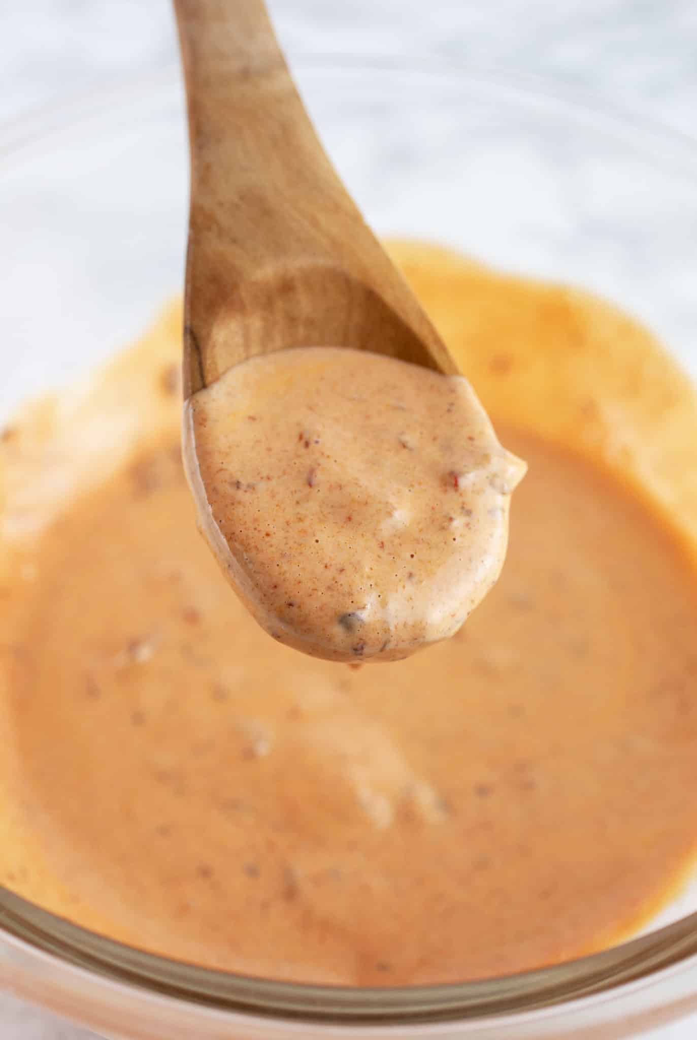 Wooden spoonful of chipotle mayo lifted from glass bowl.