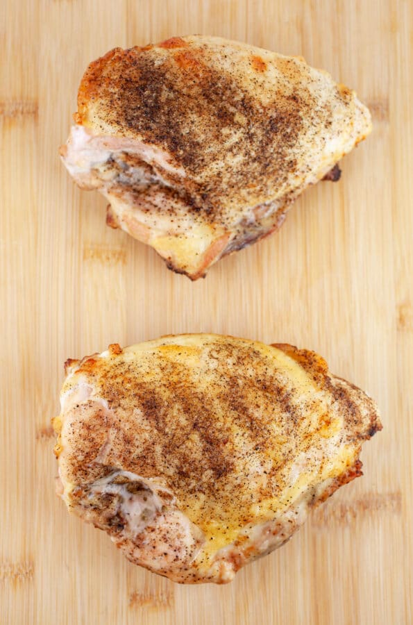 Cooked split chicken breasts on wooden cutting board.