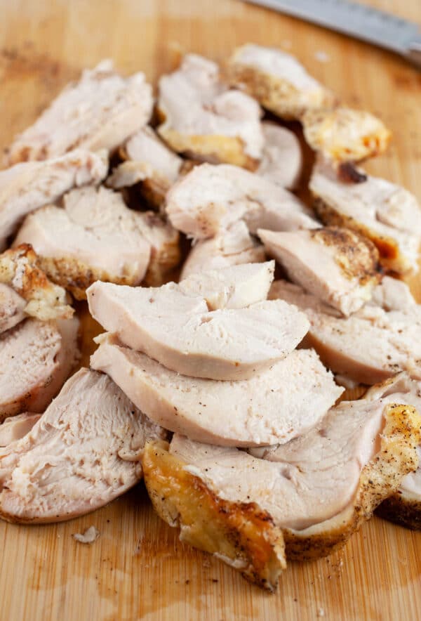 Sliced roasted split chicken breasts on wooden cutting board with knife.