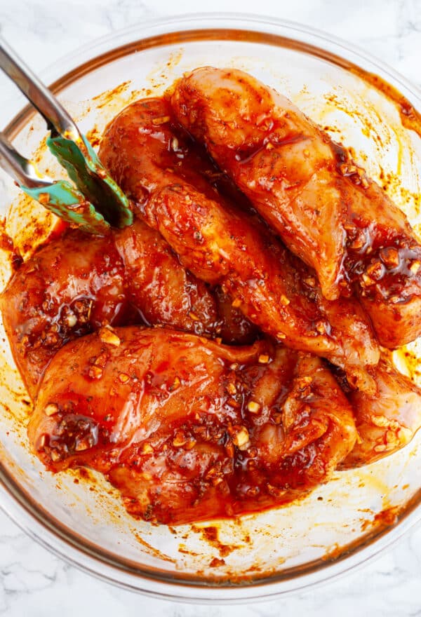 Boneless, skinless chicken breasts tossed in Southwest marinade in glass bowl with tongs.