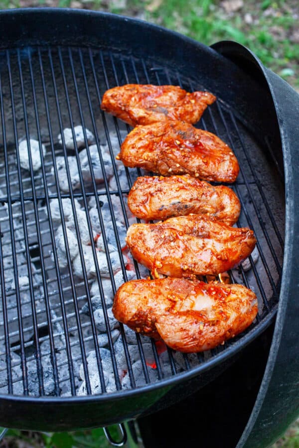 Uncooked marinated chicken breasts on charcoal grill.