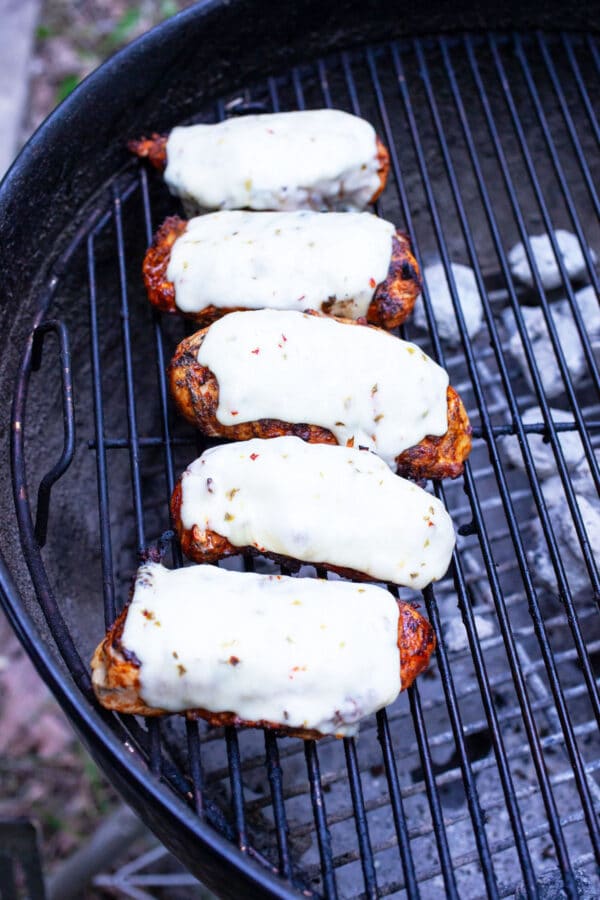 Cooked chicken breasts with Pepper Jack cheese on charcoal grill.