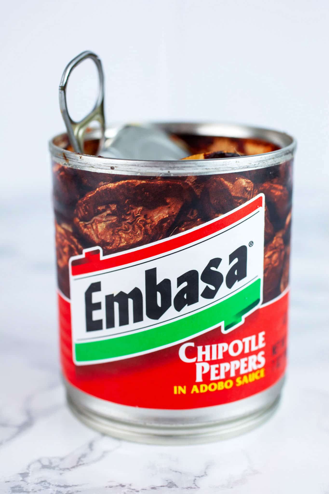 Opened can of chipotles in adobo sauce on white surface.