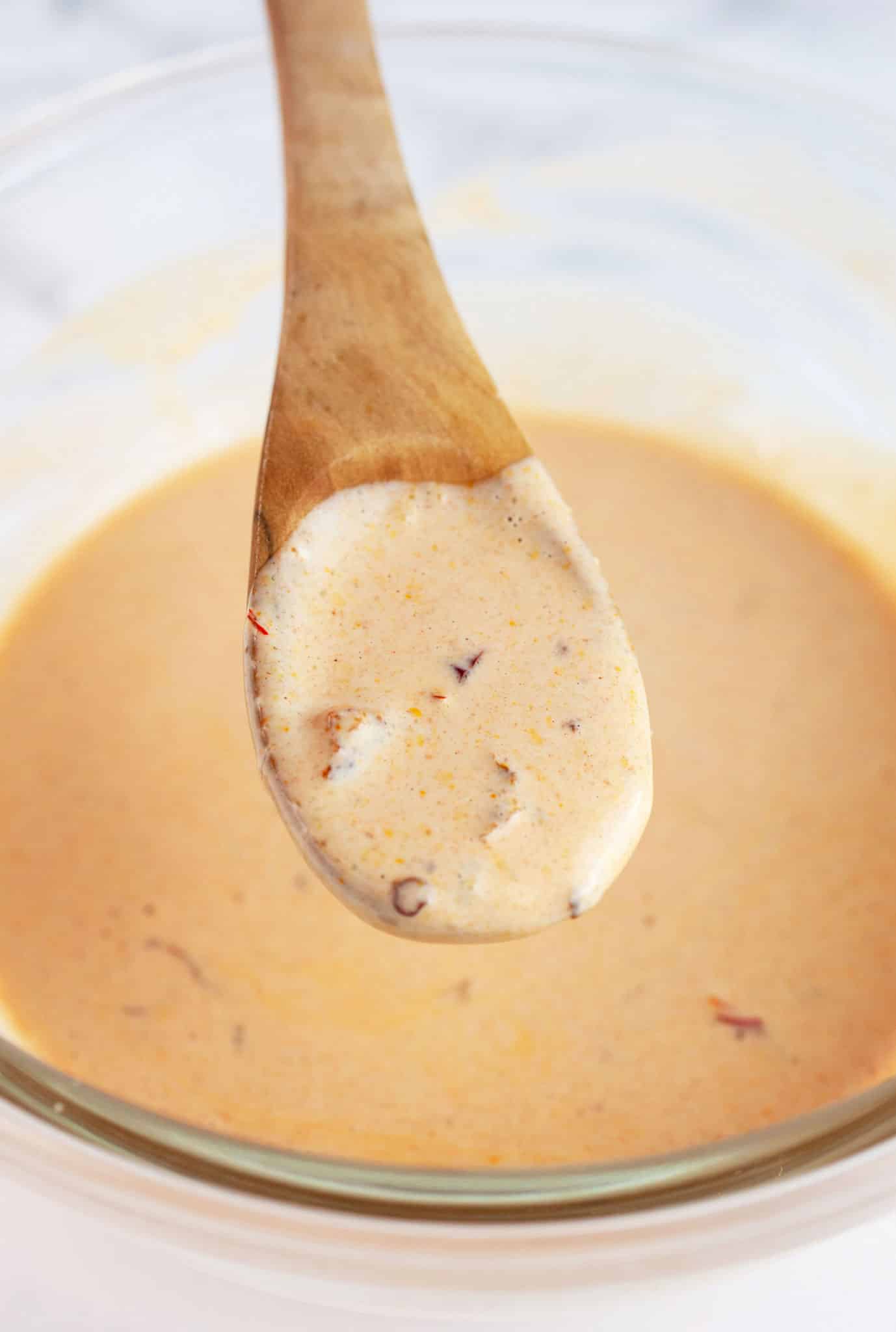 Wooden spoonful of chipotle mayo lifted from glass bowl.