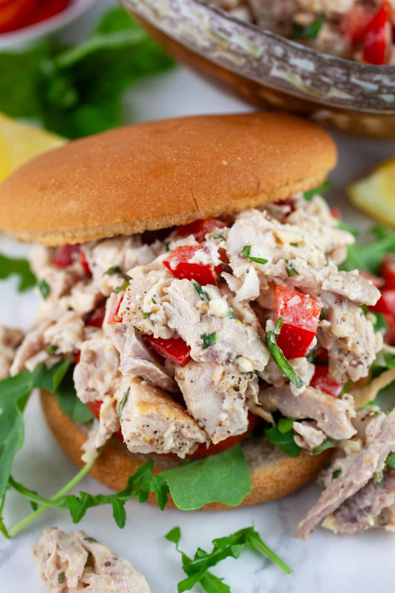 Lemon basil chicken salad with red bell peppers, tomatoes, and arugula on bun.