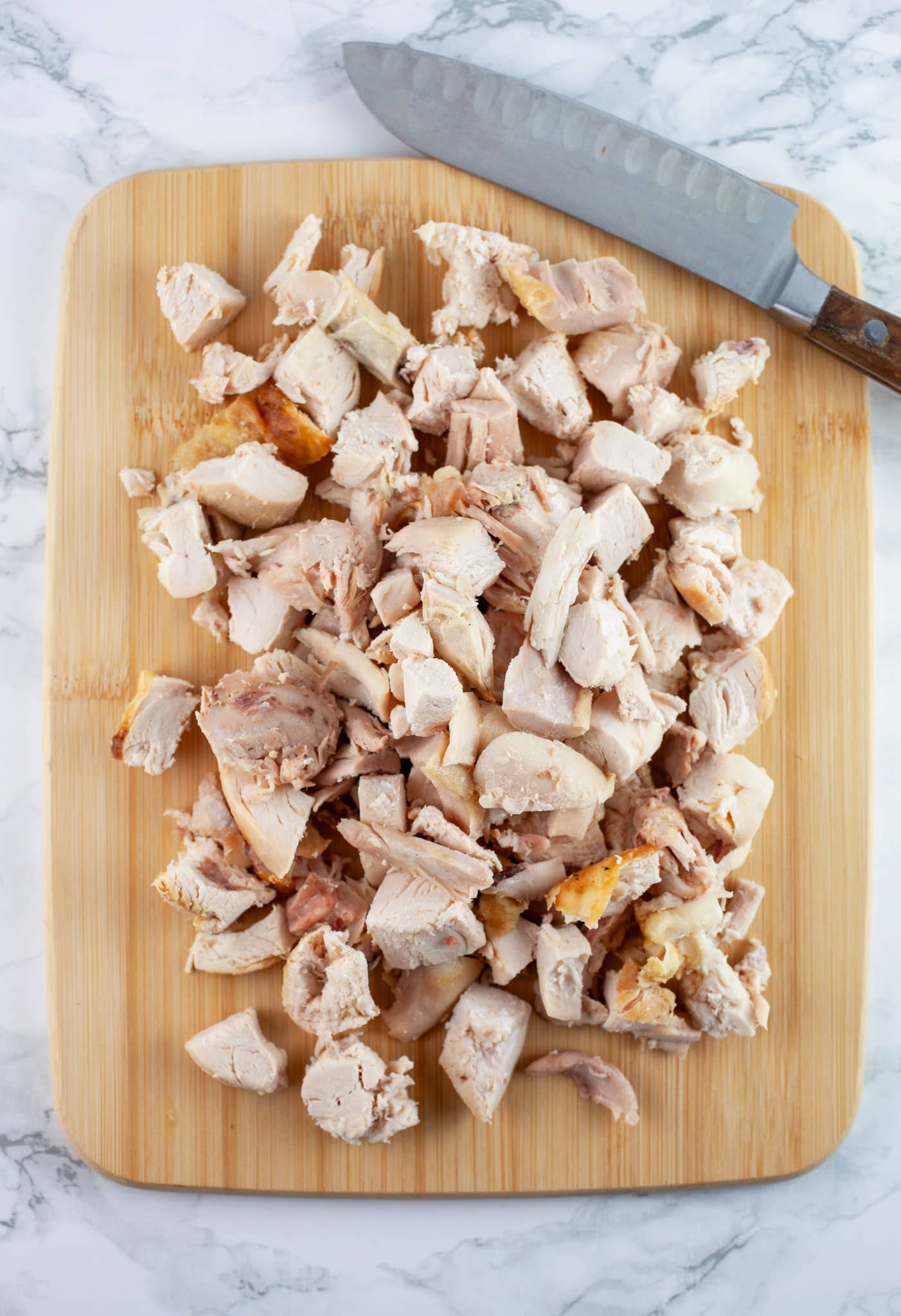 Diced rotisserie chicken on wooden cutting board with knife.