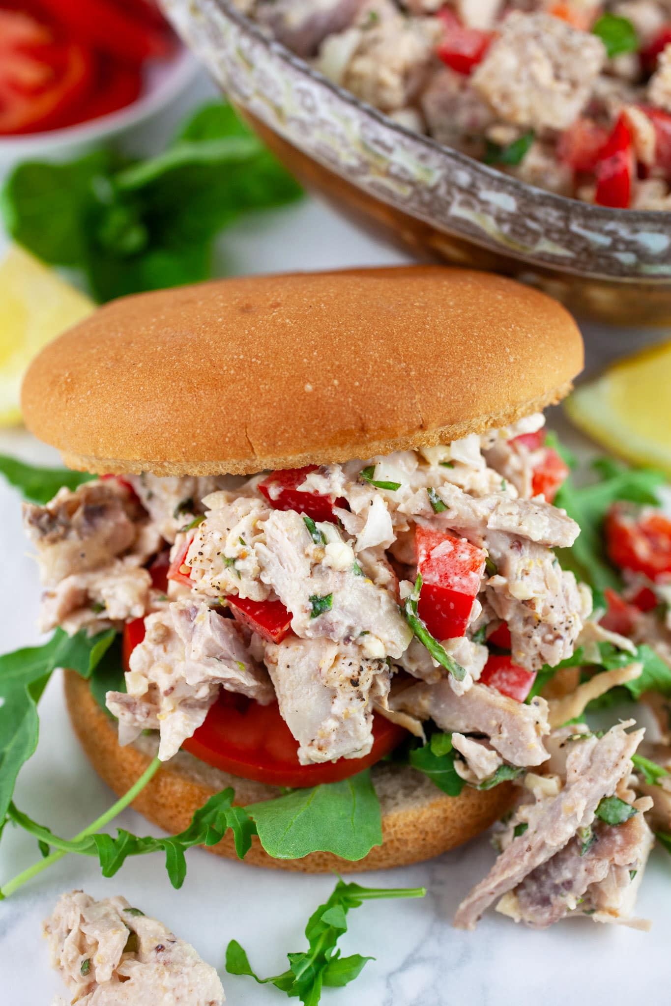 Lemon basil chicken salad with bell peppers, tomato, and arugula on bun.