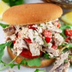 Lemon basil chicken salad with bell peppers, tomato, and arugula on bun.