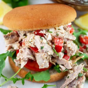 Lemon basil chicken salad with bell peppers, tomato, and arugula on bun.