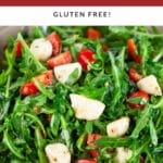 Arugula tomato mozzarella salad in ceramic bowl with spoon.