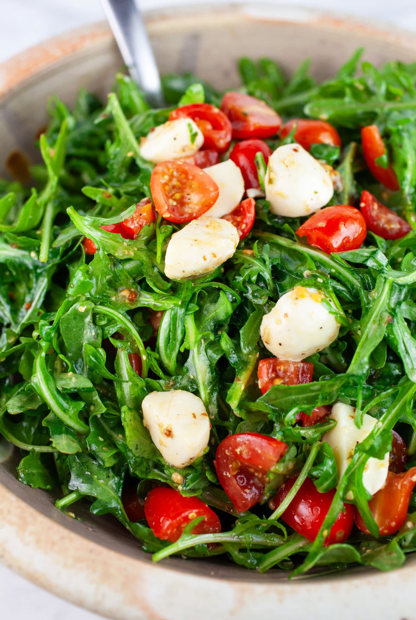 Arugula tomato mozzarella salad in ceramic bowl with metal spoon.