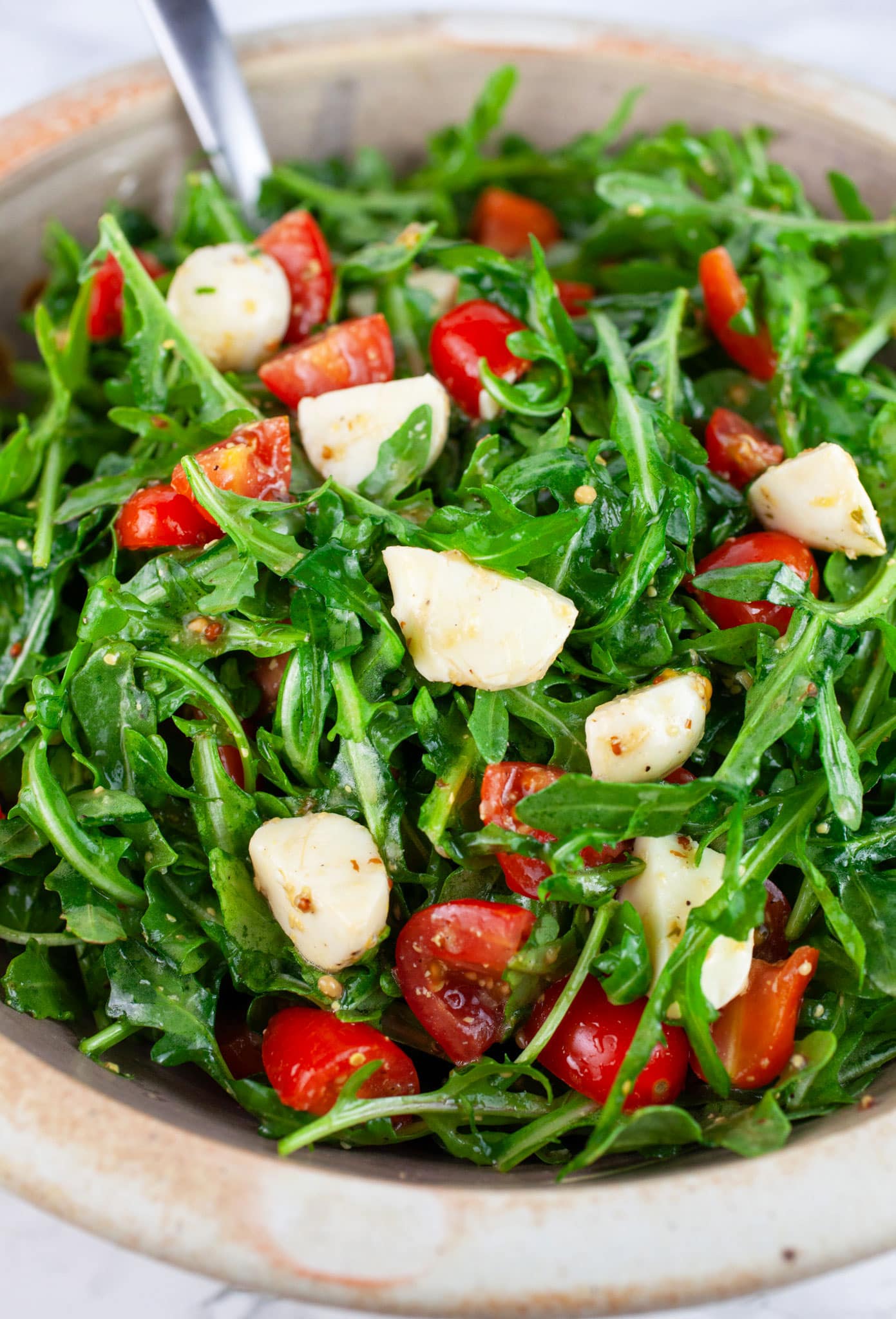Arugula tomato salad with mozzarella in ceramic bowl with metal spoon.