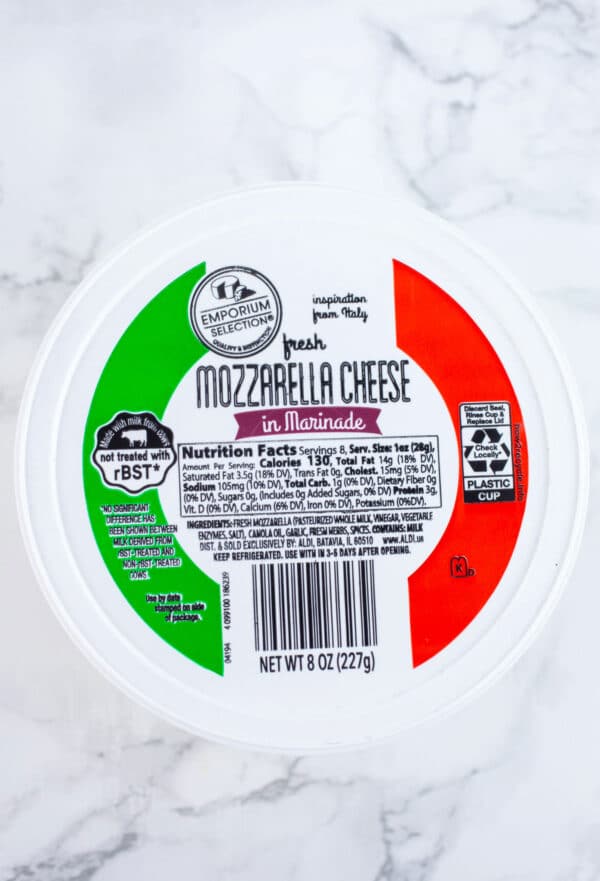 Unopened container of marinated mozzarella balls on white surface.