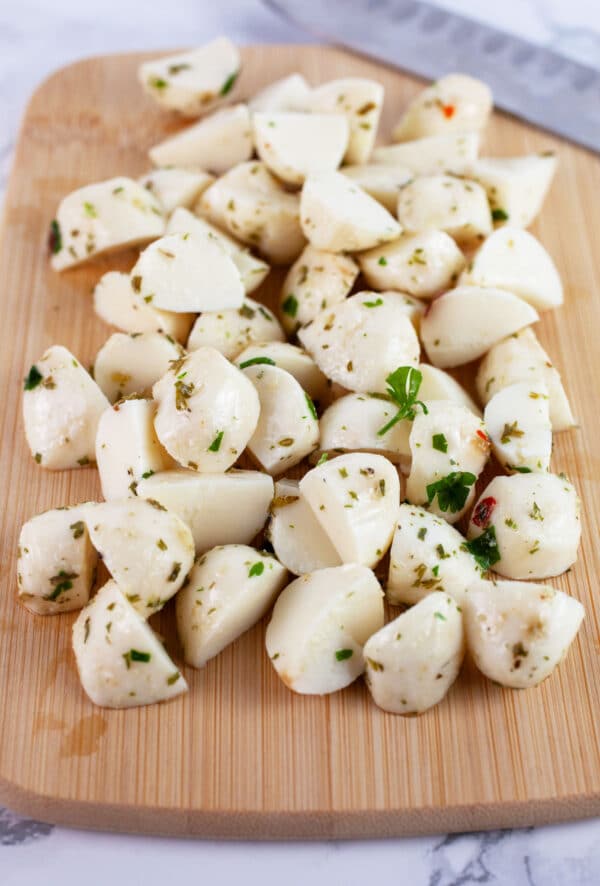 Marinated mozzarella balls cut into halves on wooden cutting board with knife.