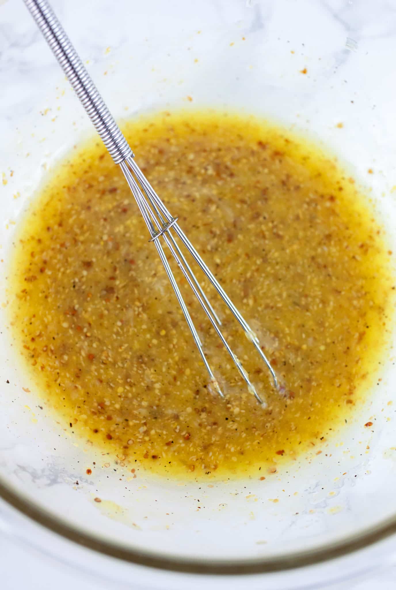 Vinaigrette dressing in glass bowl with small whisk.