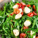 Arugula tomato mozzarella salad in ceramic bowl with metal spoon.