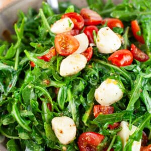 Arugula tomato mozzarella salad in ceramic bowl with metal spoon.