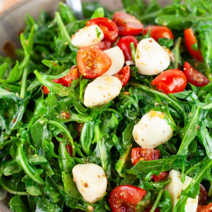 Arugula tomato mozzarella salad in ceramic bowl with metal spoon.